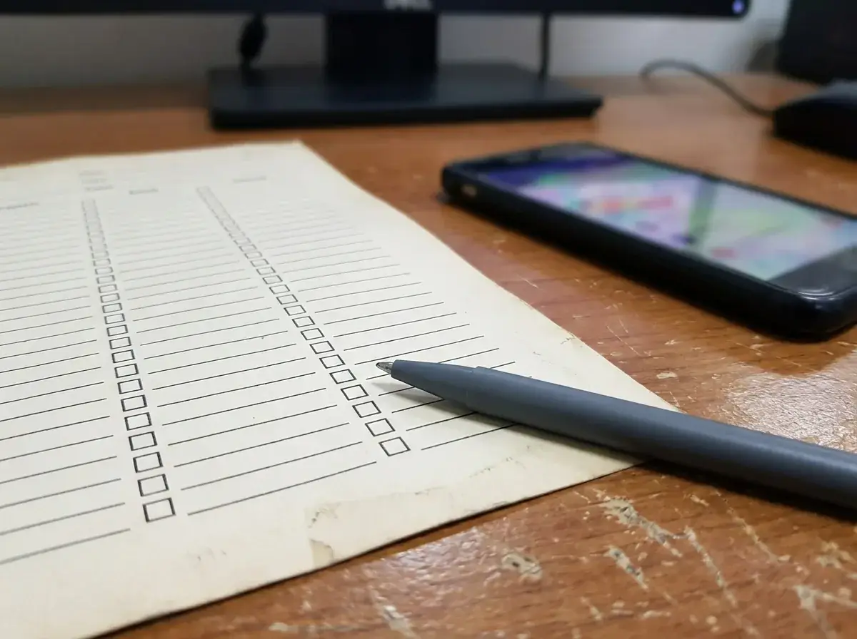 Hands logging a lead on a checklist while holding a smartphone at a contractor office desk